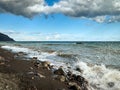 small waves roll on the rocky shore, splashes of water, blue sky with clouds Royalty Free Stock Photo