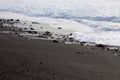 Small waves rolling onto a black sand beach strewn with rocks and pebbles in Hana Bay, Maui, Hawaii Royalty Free Stock Photo