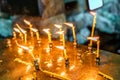 Small wax candles stuck in a tray burn outdoors at blowing wind. Orthodox Christianity religious tradition to set flaming candles