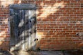 A small weathered wooden door in an old brick wall in dappled sunlight