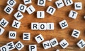 Small white and black bead cubes on wooden board, letters in middle spell ROI - Return on investment concept Royalty Free Stock Photo