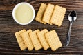 Small bowl with condensed milk, rows of cookies, spoon on wooden table. Top view Royalty Free Stock Photo