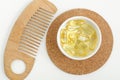 Small white bowl with cosmetic oil serum, cod fish oil capsules and wooden hair comb. Natural spa, hair care and beauty