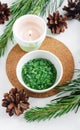 Small white bowl with green aroma bath salts, burning candle and pine branches. Christmas aromatherapy. Winter spa Royalty Free Stock Photo
