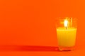 Small white candle lit in a clear glass with a vibrant orange background Royalty Free Stock Photo