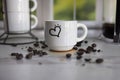 Small white ceramic espresso cup with heart drawn on it scattered coffee beans