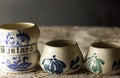 SMALL WHITE CERAMIC POTS WITH DECORATIVE BLUE MOTIFS AND A MUSTARD POT ON WHITE PAPER DOILY