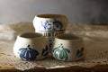 SMALL WHITE CERAMIC POTS WITH DECORATIVE BLUE MOTIFS ON WHITE PAPER DOILY