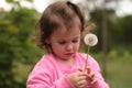 A small white child holds a dandelion in his hands while standing on a background of blurred greenery Royalty Free Stock Photo