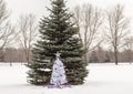 Small white christmas tree with purple and silver decorations standing in snow Royalty Free Stock Photo
