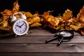 Small white clock, magnifying glass next to autumn leaves on a natural wooden table Royalty Free Stock Photo