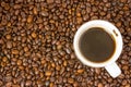 Small white cup of brewed coffee with steam above it standing on a background of scattered brown roasted coffee beans Royalty Free Stock Photo