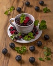 A small white cup on a saucer and wooden cutting board is filled with berries and green leaves Royalty Free Stock Photo