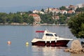 Small white and dark red boat tied to large stone and two buoys in local bay surrounded with calm sea and multiple family houses Royalty Free Stock Photo