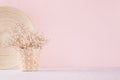 Small white dried flowers in beige wicker basket and bamboo plate on soft pink pastel background.