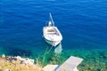 A small white fishing boat tied at the pier. White boat in the blue clear sea, picturesque photo. The boat stands near the shore