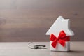 Small white house decorated red bow ribbon with bunch of keys on wooden background. Gift, real estate or buying a new home Royalty Free Stock Photo