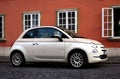 Small white Italian made 500 cc car on old city street in Europe with stucco facade.