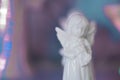 Small white marble figurine of an angel on a pearlescent pink blue blurred bokeh background.