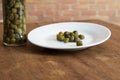 Small white plate with capers and glass with preserved capers