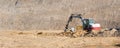 Small white and red excavator moving earth in the middle of a large construction site to build a new road and access to the city. Royalty Free Stock Photo