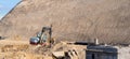 Small white and red excavator moving earth in the middle of a large construction site to build a new road and access to the city. Royalty Free Stock Photo