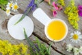 Small white scoop with cosmetic/cleansing oil and cotton pad for natural skin care. Old wooden background with field flowers.