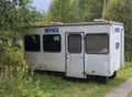 Small white trailer house with blue sign office, abandoned caravan in rural landscape near footpath, green grass and trees Royalty Free Stock Photo