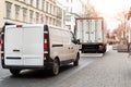 Small white van and mid size cargo truck parked for unloading at european old city street road. Fast express courier