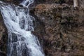 small white waterfall tumbles over dark rock wall Royalty Free Stock Photo
