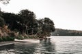 small white wooden canoe with oars standing on the shore of calm water lake near the path leading to forest and trees Royalty Free Stock Photo