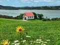 A small white wooden church building on an estuary shove with a green lawn and flowers on the foreground on the Royalty Free Stock Photo