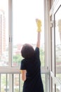 Small woman with difficulty washes high windows on the balcony.