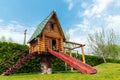 Small wood log playhouse hut with stairs ladder and wooden slide on children playground at park or house yard. Green grass lawn Royalty Free Stock Photo