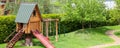 Small wood log playhouse hut with stairs ladder and wooden slide on children playground at park or house yard. Panoramic Royalty Free Stock Photo