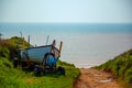 A small wooden boat is left on a towing wagon by a dirt path near the ocean Royalty Free Stock Photo