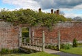 Small wooden bridge with an interesting open pattern crosses a stream and leads into a walled garden Royalty Free Stock Photo