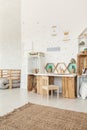 Small wooden chair standing by the desk and crate shelves in white Scandi baby girl room interior with carpet and posters on Royalty Free Stock Photo
