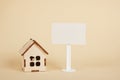 Small wooden house model and white blank sign for inscription on beige background copy space Royalty Free Stock Photo