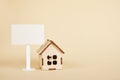 Small wooden house model and white blank sign for inscription on beige background copy space Royalty Free Stock Photo