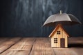 Small wooden house under umbrella on the table, gray background, copy space. Home insurance concept. AI generated Royalty Free Stock Photo