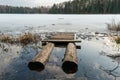 Wooden pier made of two logs and planks. Melted ice near the shore on the lake in the woods. Evening time in early spring Royalty Free Stock Photo