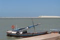 Small wooden sailboat moored at a pier in a bay and in the background a sand dune Royalty Free Stock Photo