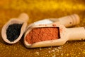 Small wooden spoons with black sesame, salt and papic on a yellow shiny background