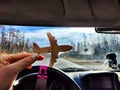 Small wooden toy airplane in the female driver& x27;s hand in a car on the background of the road and highway. The Royalty Free Stock Photo