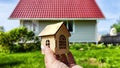 Small wooden toy house on palm of woman hand and big home on background. symbol and concept of cconstruction, buying Royalty Free Stock Photo