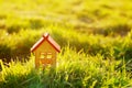 A small wooden toy house stands on the palm of a female hand against a background of green grass in the sunlight Royalty Free Stock Photo