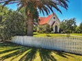 Small wooden village church with white fence and phoenix palm on the foreground in New Zealand