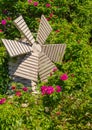 A small wooden windmill in the beautiful summer garden. Windmill and roses. Garden furniture Royalty Free Stock Photo