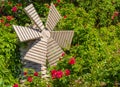 A small wooden windmill in the beautiful summer garden. Windmill and roses. Garden furniture Royalty Free Stock Photo